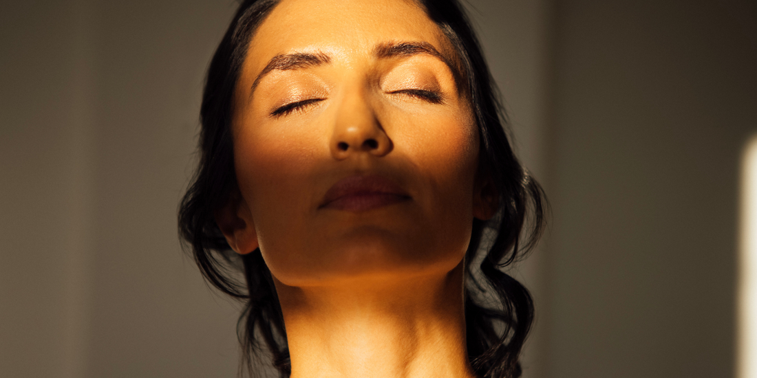 Жена със затворени очи, осветена от топла слънчева светлина върху лицето, символизираща пролетно възстановяване на кожата и естествена грижа за кожата.