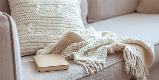 Уютен зимен интериор с мек плед и книга върху светъл диван, създаващ усещане за спокойствие и почивка у дома
