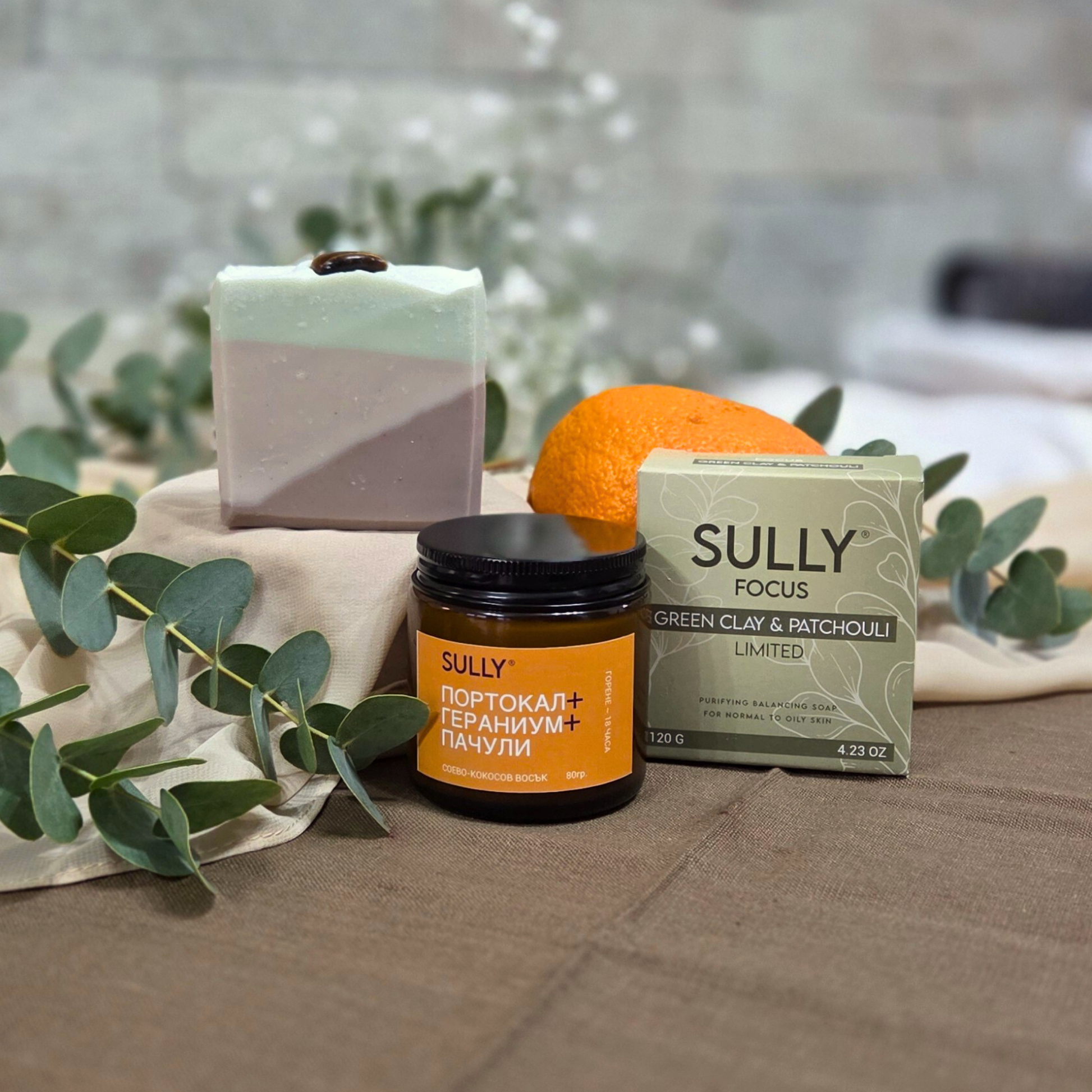 Комплект „Душ и аромат“ с кристален сапун FOCUS (зелена глина и пачули) и соева свещ „Портокал, гераниум и пачули“, с портокал и евкалипт на фон.
