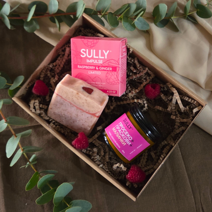 Подаръчна кутия с кристален сапун IMPULSE (малина и джинджифил) и соева свещ „Просеко, праскови и малинки“, подредени в крафт кутия с пълнеж, малини и евкалипт на фон.