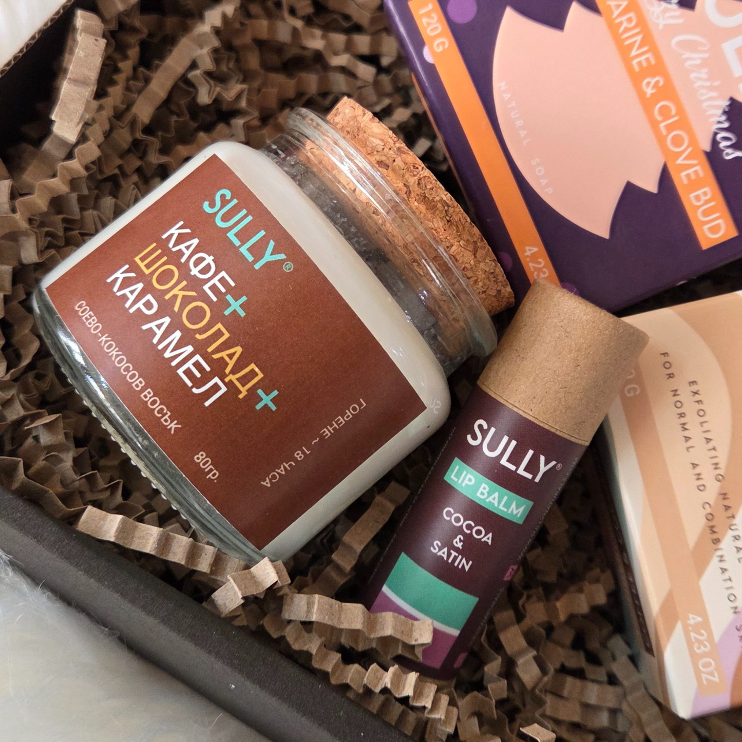 Коледен комплект „Сутрешен уют“ SULLY Naturals с ароматна свещ, сапуни и балсам за устни в празнична кутия.