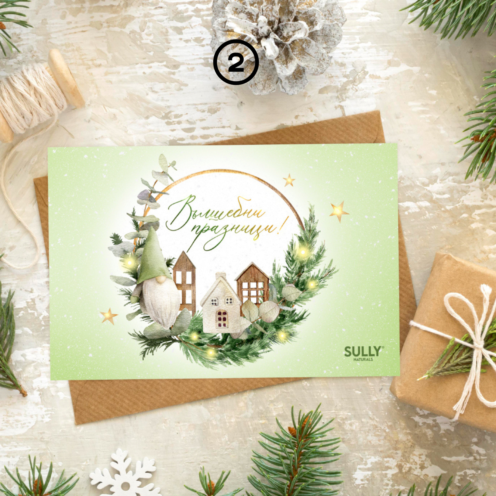 Коледна картичка „Вълшебни празници“ SULLY Naturals с илюстрация на малко градче, венец и надпис в зелено, поставена върху крафт плик.
