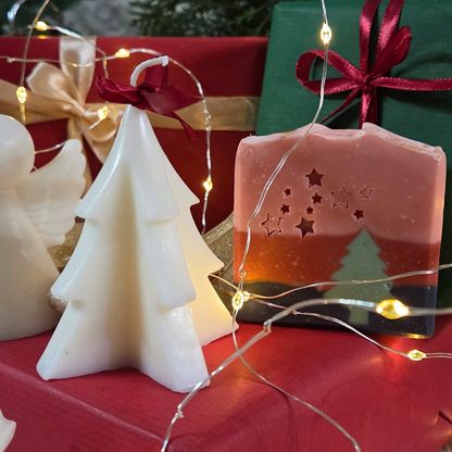 Свещ във форма на елхичка до сапун „Горско вълшебство“ SULLY Naturals, обградени от коледни лампички.