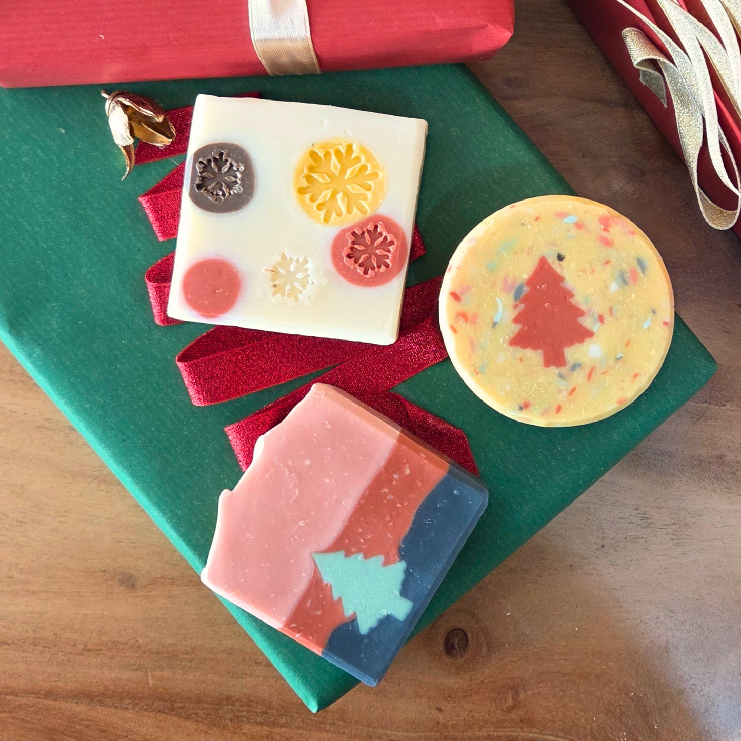 Коледен комплект натурални сапуни „Празнично трио“ SULLY Naturals, подредени върху зелена кутия с червена панделка.