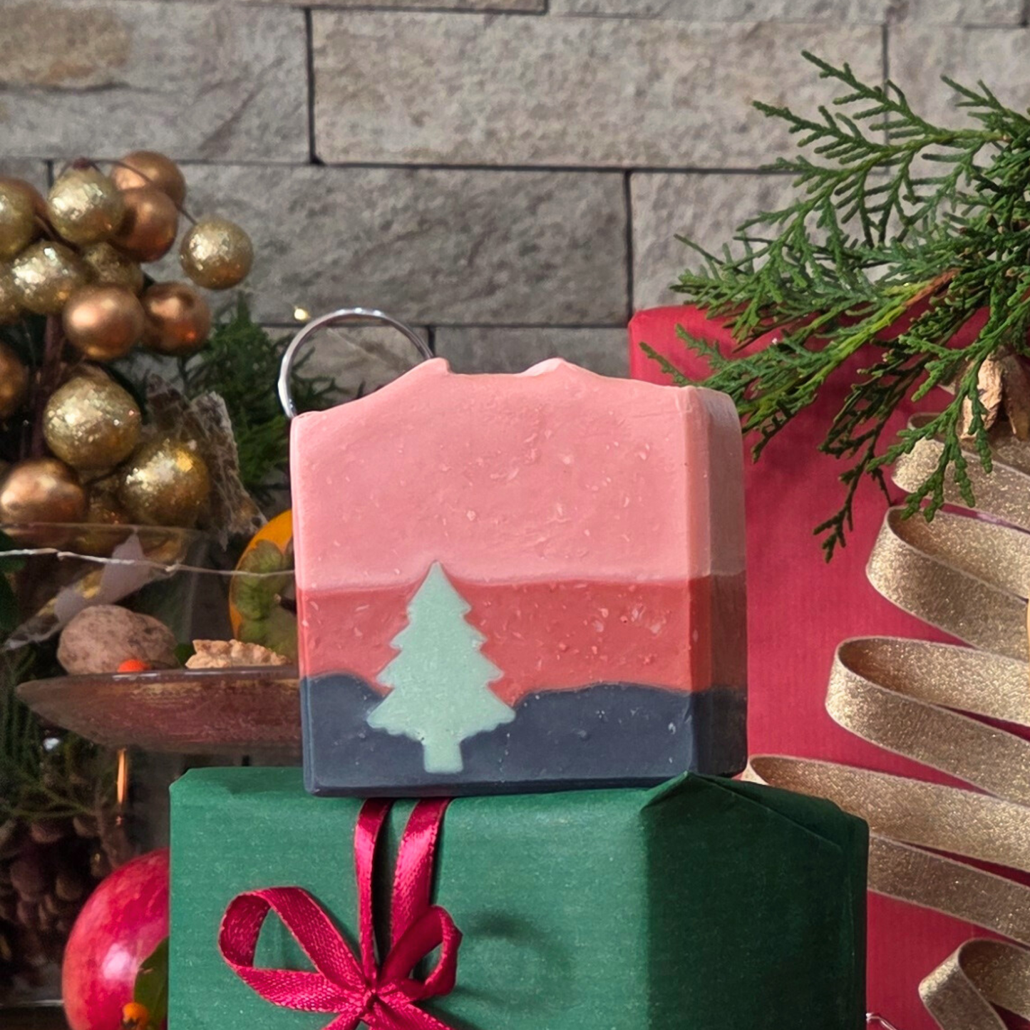 Ръчно изработен сапун „Горско вълшебство“ SULLY Naturals с вградена зелена елхичка, поставен върху зелен подарък с червена панделка.
