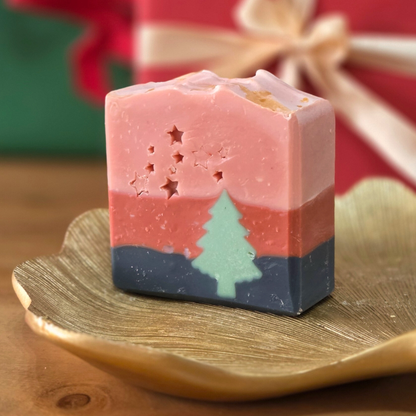 Сапун „Горско вълшебство“ SULLY Naturals с аромат на кипарис и тамян, сниман върху златен лист и коледни светлини.