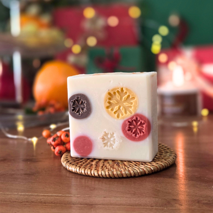 Ароматен сапун „Уютна Коледа“ SULLY Naturals с релефни снежинки в празнични цветове, сниман на фон с коледни светлини.