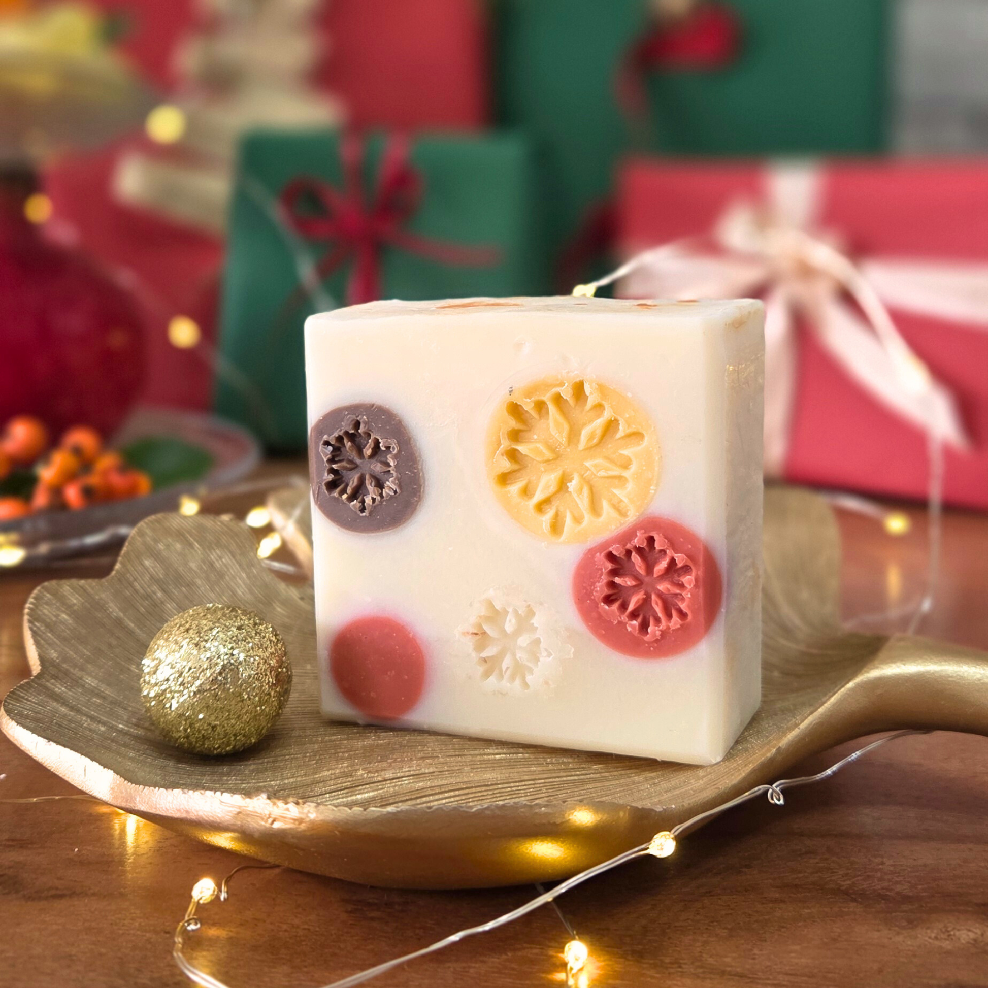 Натурален сапун „Уютна Коледа“ SULLY Naturals с мандарина и карамфил, поставен върху златен лист сред празнична украса.