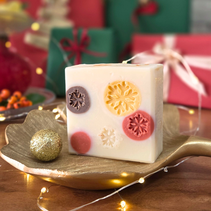 Натурален сапун „Уютна Коледа“ SULLY Naturals с мандарина и карамфил, поставен върху златен лист сред празнична украса.