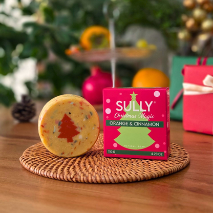 Натурален сапун „Вълшебна Коледа“ SULLY Naturals с портокал и канела, показан с празнична опаковка върху ратанова подложка.
