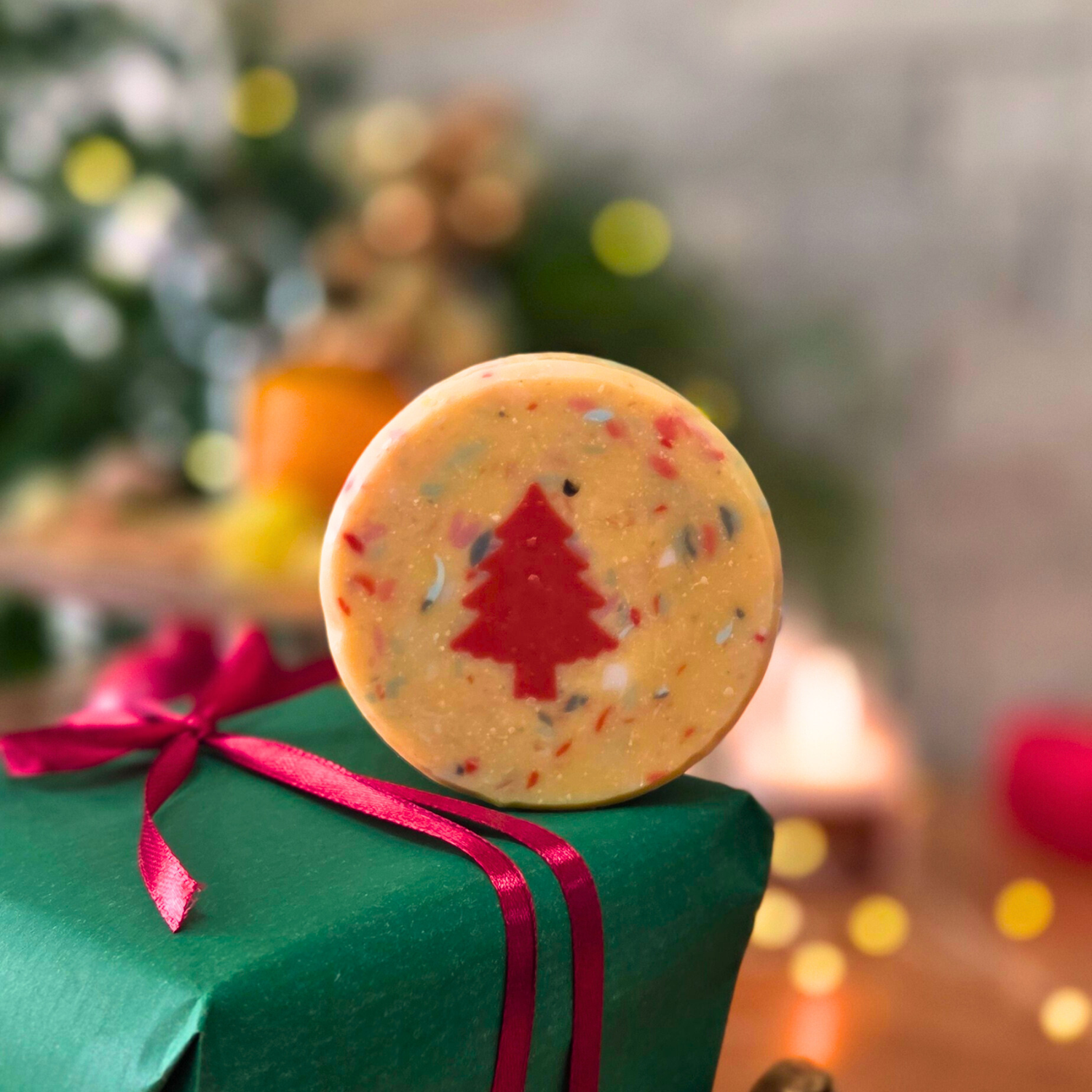 Ръчно изработен сапун „Вълшебна Коледа“ с вградена червена елхичка, поставен върху зелен подарък с червена панделка.