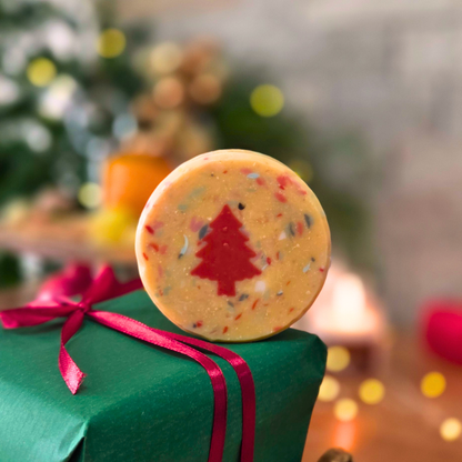 Ръчно изработен сапун „Вълшебна Коледа“ с вградена червена елхичка, поставен върху зелен подарък с червена панделка.