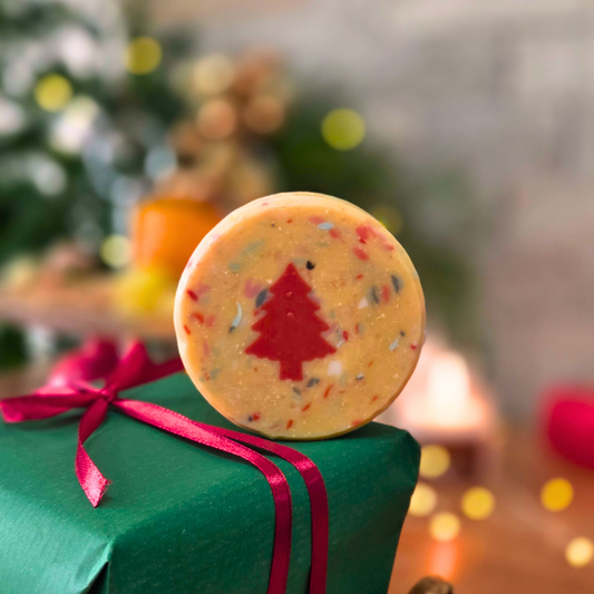 Ръчно изработен сапун „Вълшебна Коледа“ с вградена червена елхичка, поставен върху зелен подарък с червена панделка.