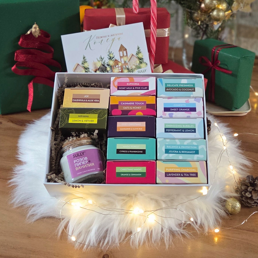 одаръчен комплект с 12 натурални сапуна SULLY в цветни опаковки, свещ и празнична картичка, подредени върху пухкав бял фон с лампички.