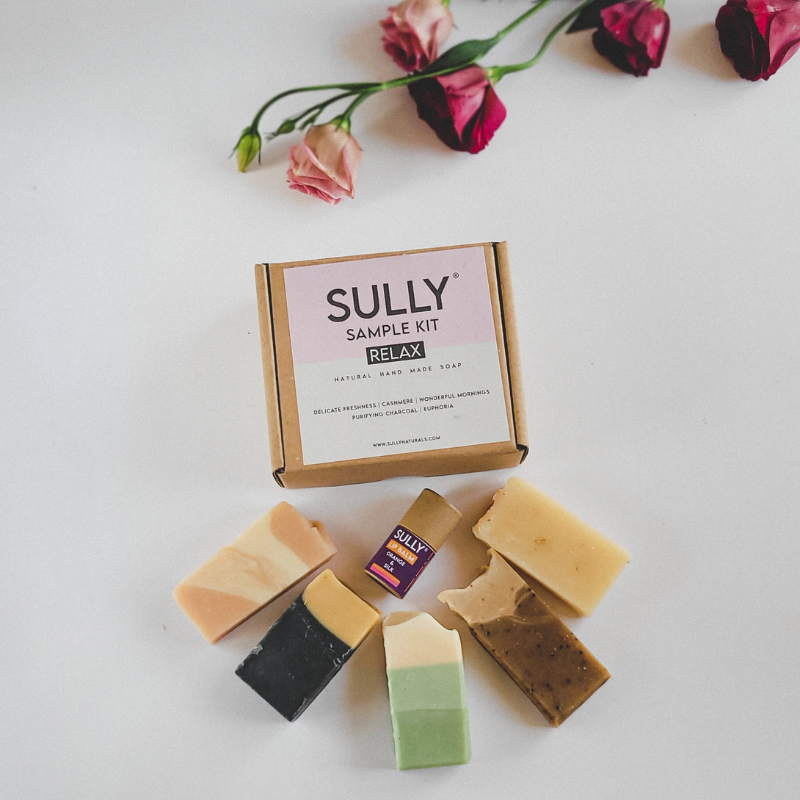 SULLY Sample Kit Relax – комплект с мини сапуни и мини балсам за устни 6 г, подредени около кутия Relax върху бял фон с цветя.