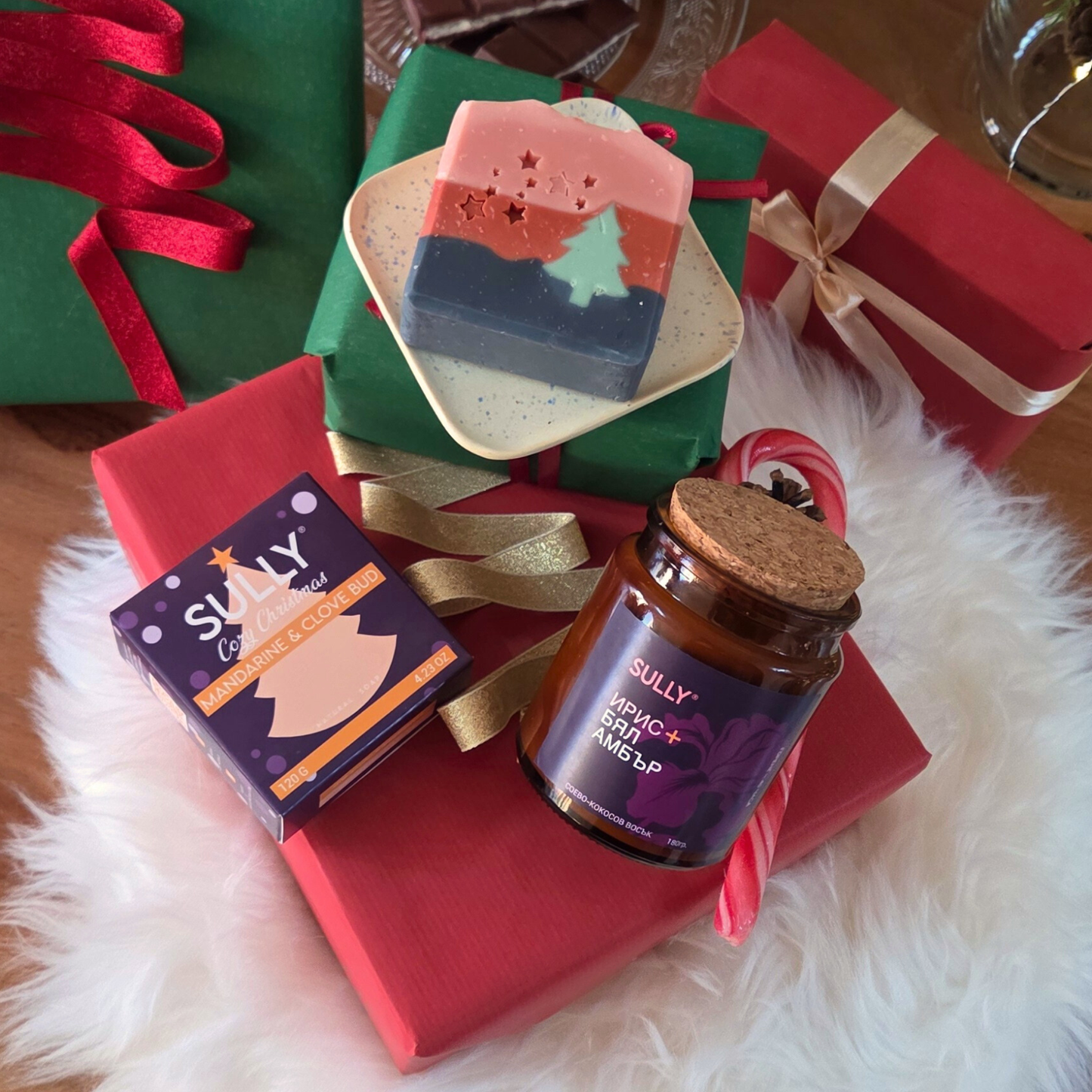 Ароматна свещ „Ирис и бял амбър“ SULLY Naturals и коледен сапун, поставени върху керамична сапунерка с подаръчна опаковка.