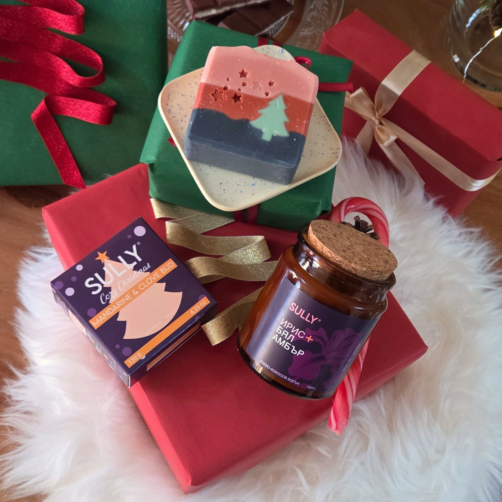 Ароматна свещ „Ирис и бял амбър“ SULLY Naturals и коледен сапун, поставени върху керамична сапунерка с подаръчна опаковка.