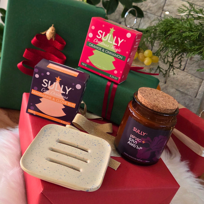 Комплект „Зимна грижа“ SULLY Naturals – керамична сапунерка, сапуни и свещ, подредени върху коледни подаръци.